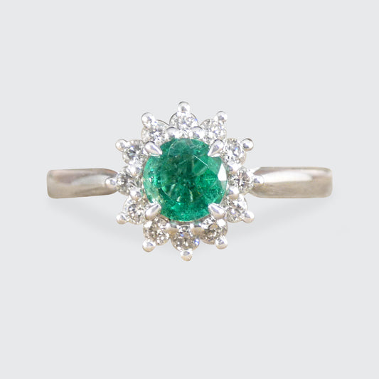 Elegant emerald and diamond flower cluster ring set in platinum, showcasing a vibrant green emerald surrounded by a sparkling halo of diamonds.