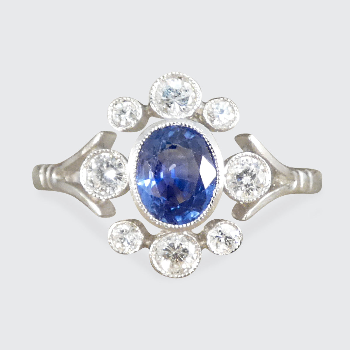 This stunning Platinum ring features a distinctive Art Deco-inspired design with a rich sapphire center surrounded by sparkling diamonds. A contemporary reproduction, it combines timeless elegance with modern craftsmanship, making it a standout piece for any collection.