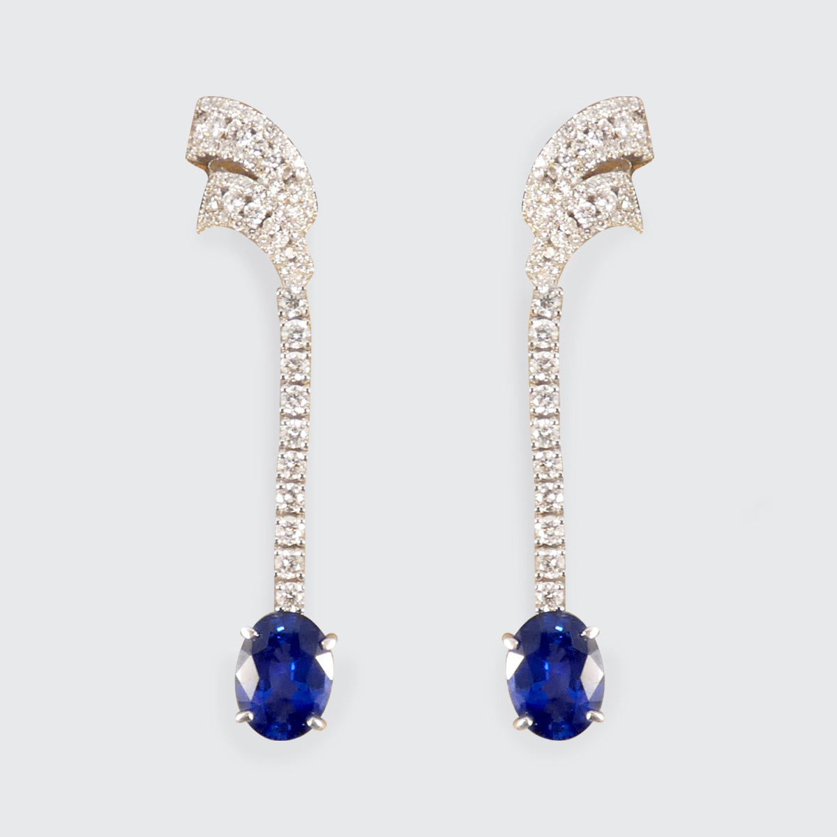 Contemporary Sri Lankan Sapphire and Diamond drop earrings featuring vibrant blue oval sapphires suspended from a line of dazzling diamonds in a sleek white gold setting.