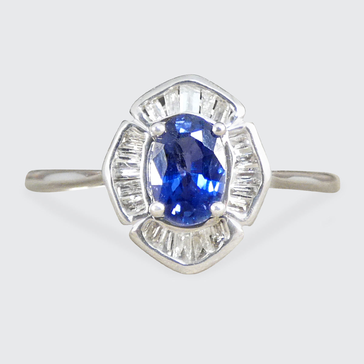 A sApphire and Diamond Cluster Ring with an Oval cut Sapphire centre in a four claw setting with a surround f tapered baguette cut diamonds.