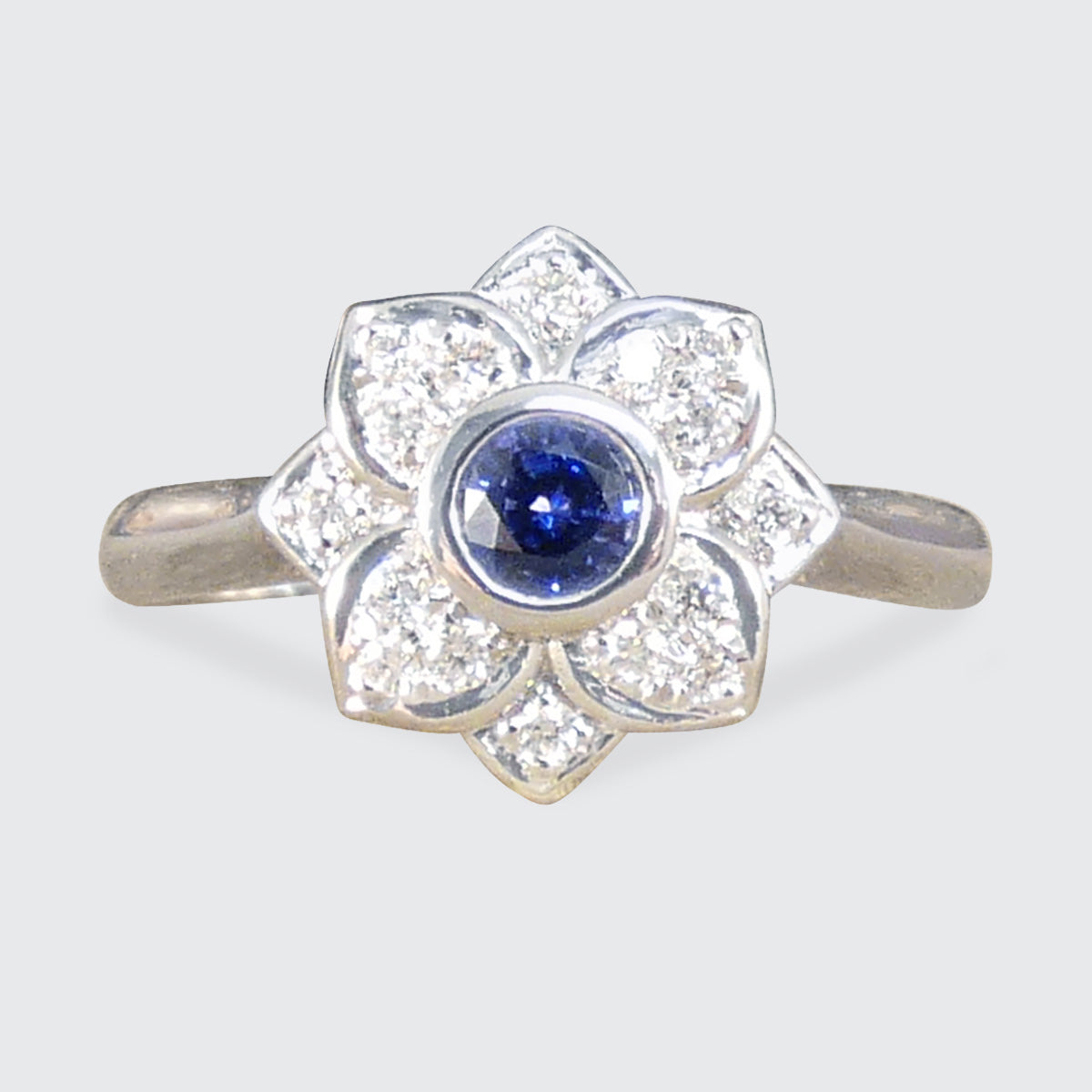 A flower cluster ring featuring a Ceylon Sapphire in the centre in a rub over bezel setting with a petal shaped Diamond clusters all made in Platinum.