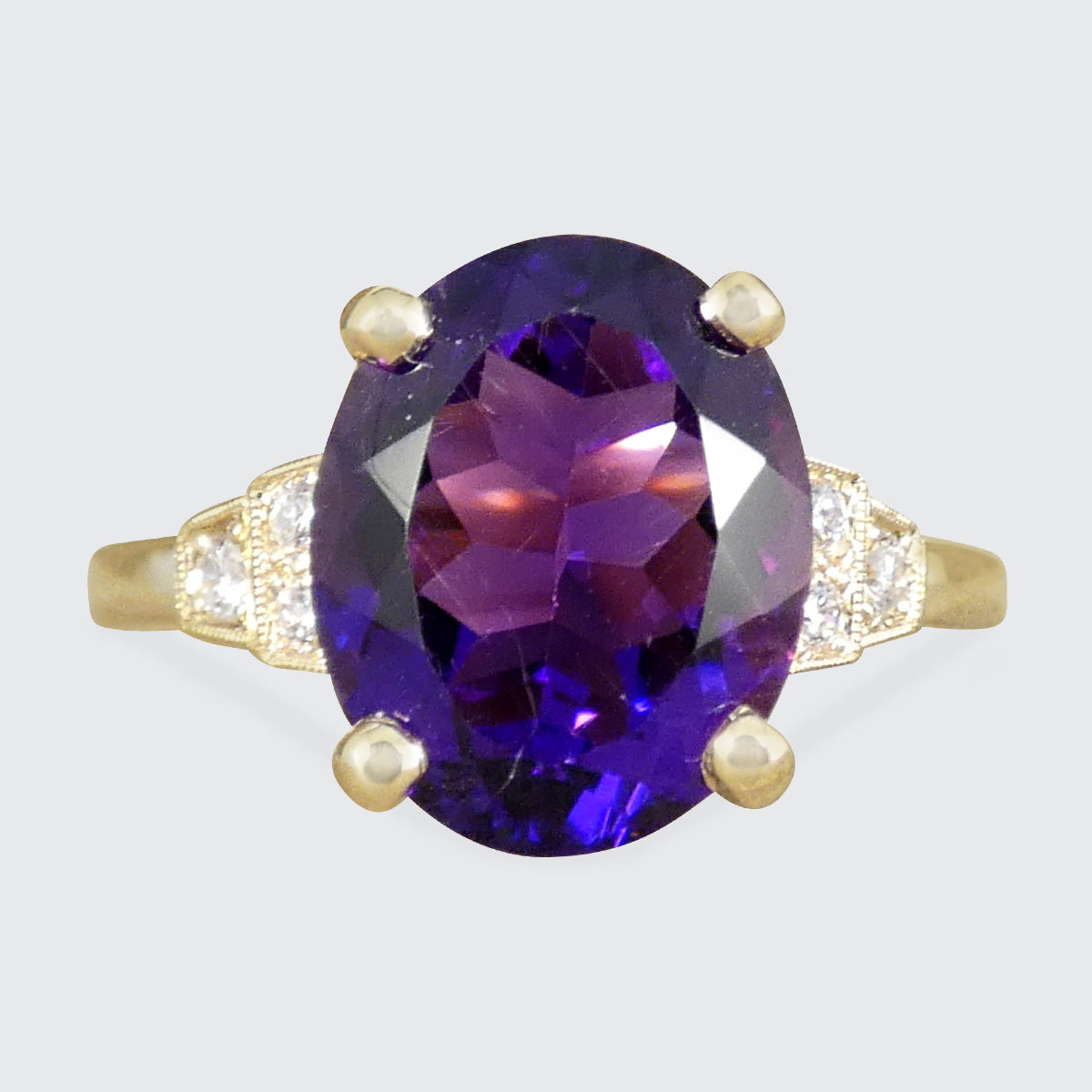 Bright and vibrant amethyst ring in a four claw setting with diamond set shoulders in 9ct yellow gold.