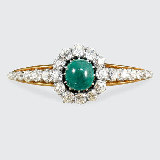 Late Victorian cabochon emerald and diamond bangle featuring a central vibrant green emerald surrounded by old-cut diamonds, set in an elegant yellow gold design.