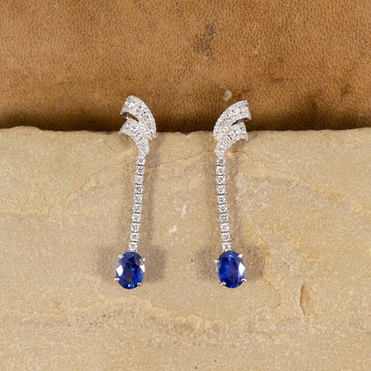 Contemporary Sri Lankan Sapphire and Diamond drop earrings featuring vibrant blue oval sapphires suspended from a line of dazzling diamonds in a sleek 18ct white gold setting.