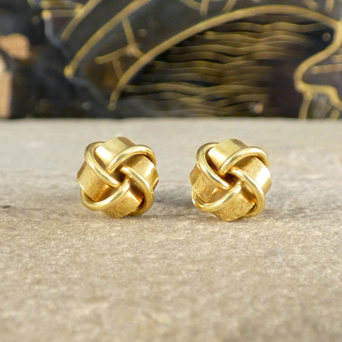 Pair of vintage knot earrings in 9ct yellow gold displayed on a textured background. These timeless earrings feature a beautifully intertwined design, exuding elegance and a classic appeal for any occasion.