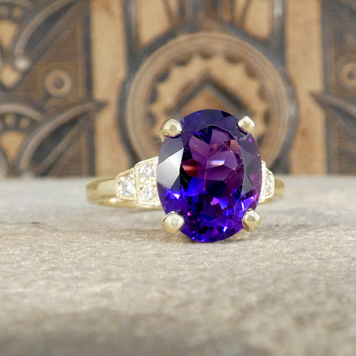 Bright and vibrant amethyst ring in a four claw setting with diamond set shoulders in 9ct yellow gold.