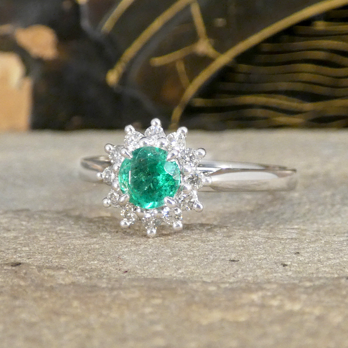 Elegant emerald and diamond flower cluster ring set in platinum, showcasing a vibrant green emerald surrounded by a sparkling halo of diamonds.