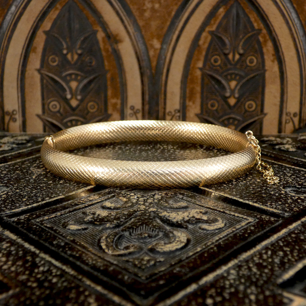 Vintage hollowed 9ct yellow gold bangle with a textured finish, elegantly placed on a decorative Gothic-style surface.