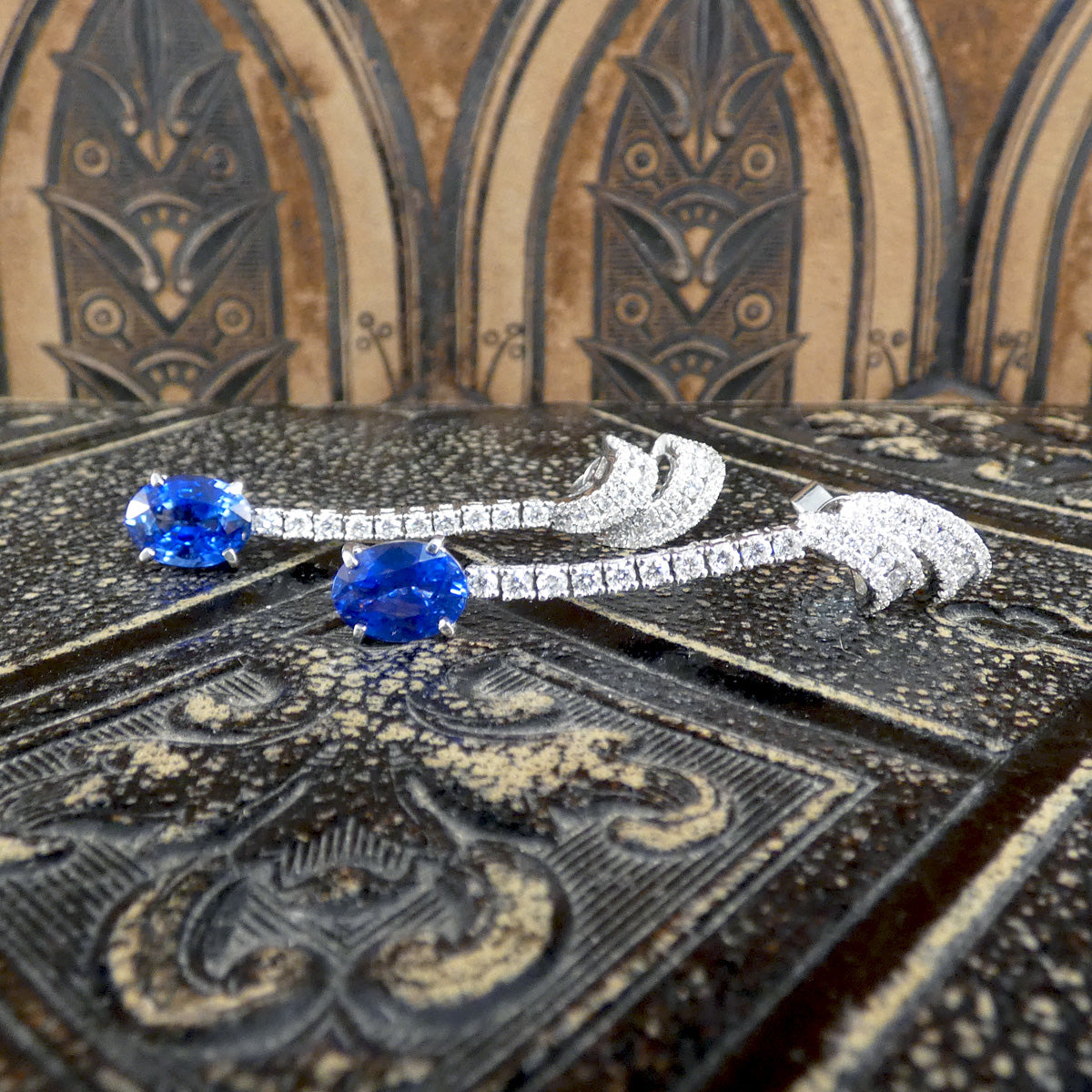 Contemporary Sri Lankan Sapphire and Diamond drop earrings featuring vibrant blue oval sapphires suspended from a line of dazzling diamonds in a sleek white gold setting. Showing bright and vivid blue colour to the Sapphires.