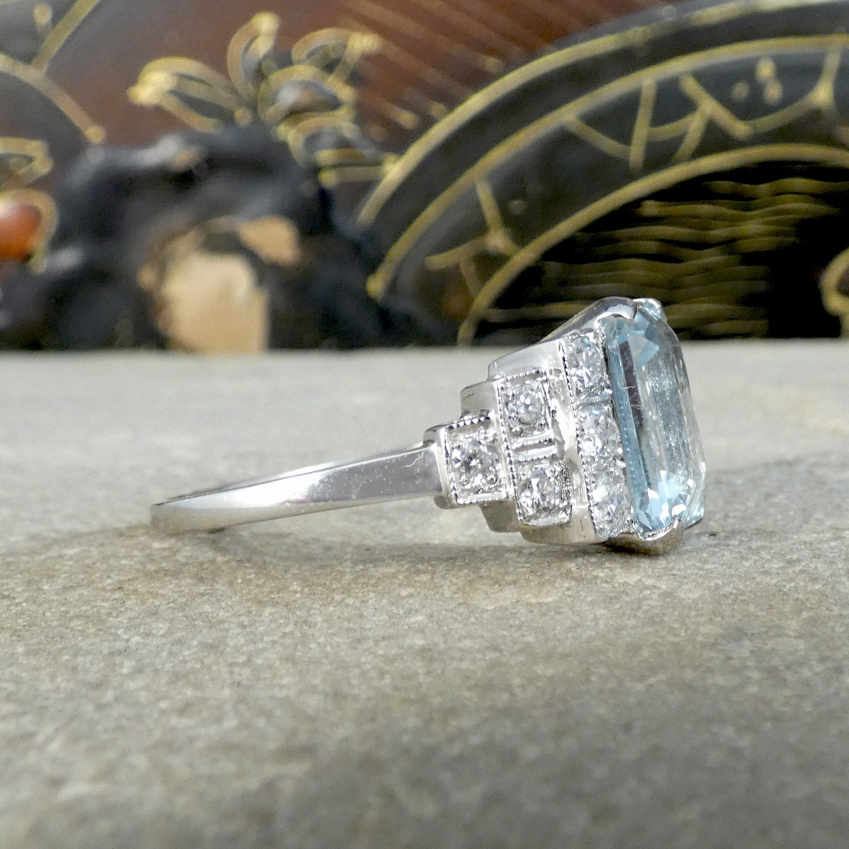 An Art Deco style ring that has been newly crafted with a 3.00ct light blue Aquamarine with graduated staged set Diamond shoulders in Platinum. Showing from the side and highlighting the milgrain edge detail typical of Deco jewellery.