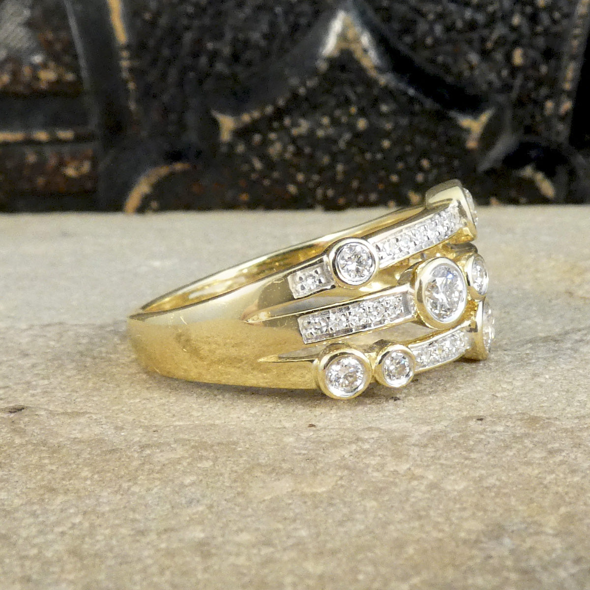 A modern bubble style diamond set ring. With larger and smaller Diamonds bezel set into three bands across a the head of the ring. Made in 9ct Yellow Gold. Shown from side view to see how far the Diamond spread around the finger.