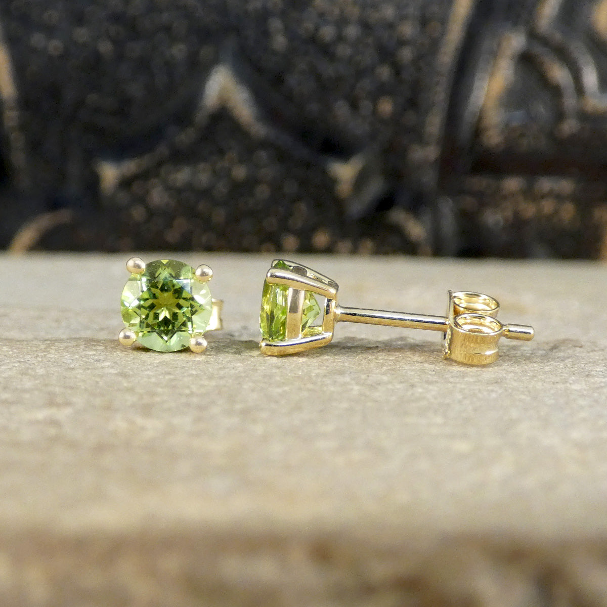 Four-claw peridot stud earrings crafted in 9ct yellow gold, featuring vibrant round-cut green gemstones with a classic and elegant design. One profile and one front on.