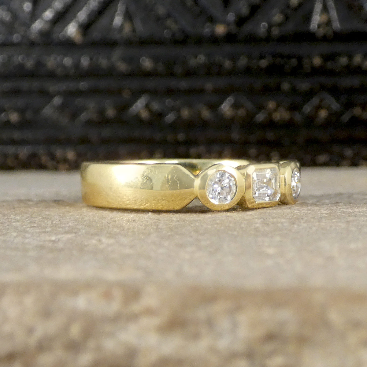 Side view of a half eternity ring featuring bezel-set emerald-cut and brilliant-cut diamonds in 18ct yellow gold, showcasing the ring's sleek profile and elegant design.