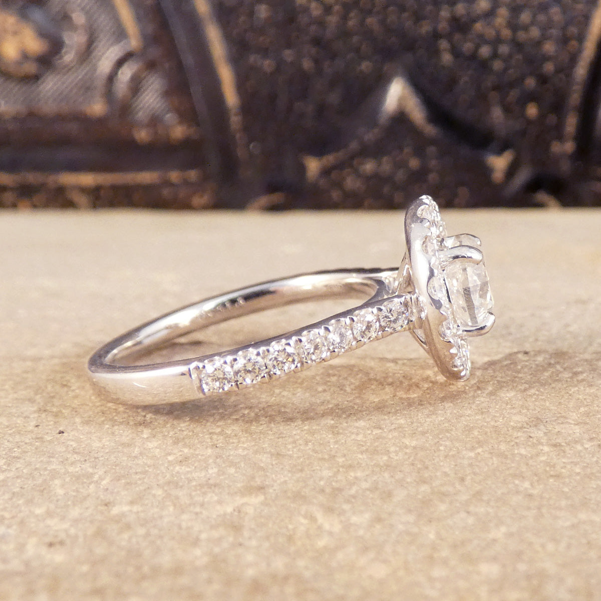 Side view of halo diamond engagement ring with diamonds set into each shoulder. Showing how far the diamonds are set around each side leading to a plain polished band.