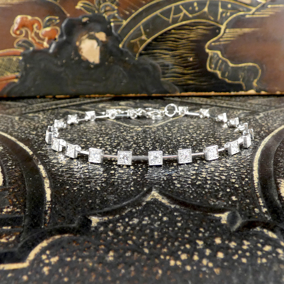 Full view of an 18-carat white gold tennis bracelet featuring square bezel-set diamonds with a total weight of 1.50 carats. The elegant and contemporary design is beautifully displayed on a textured surface, making it a luxurious accessory for any occasion and perfect gift.