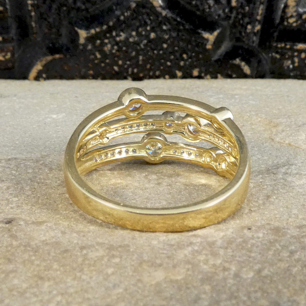 Back view of a modern bubble style diamond set ring. With larger and smaller Diamonds bezel set into three bands across a the head of the ring all made in Yellow Gold with a comfortable feel.