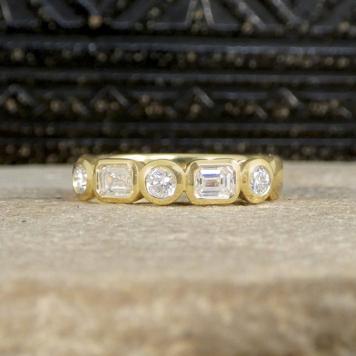 Half eternity ring with alternating emerald-cut and brilliant-cut diamonds, bezel set in 18ct yellow gold, offering a modern and sophisticated design.