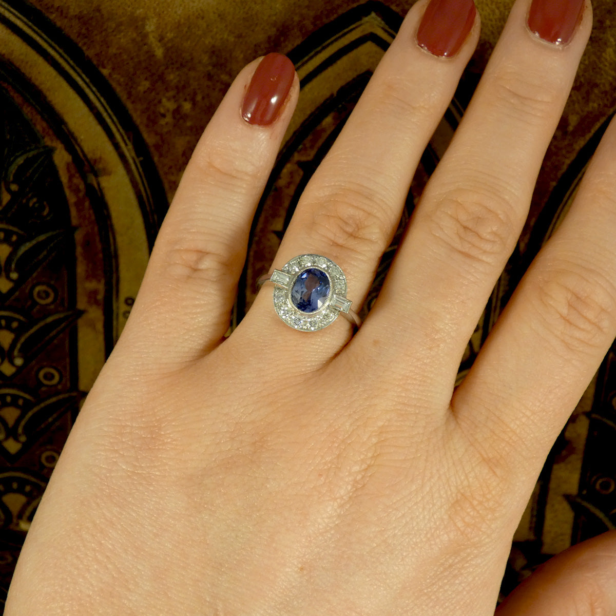 An oval cut Sapphire with a rub over bezel setting surrounded by Brilliant and Baguette cut Diamonds clustering the velvet blue centre stone. A true are deco style ring, a beautiful vintage classic shown on the finger to see what it looks like worn.