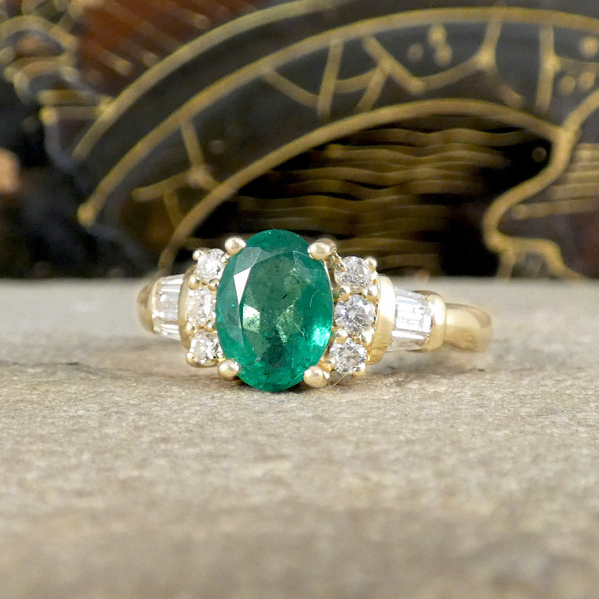 Emerald ring with three brilliant cut diamonds clustering on the east and west of the Emerald sowing a bright and sparkly appearance.