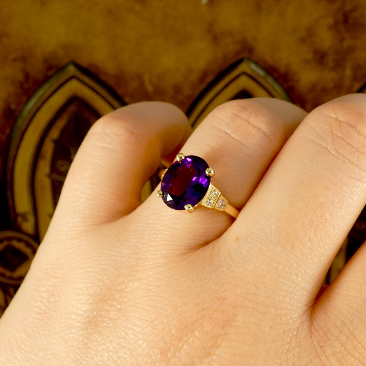 Bright and vibrant amethyst ring in a four claw setting with diamond set shoulders in 9ct yellow gold. Shown on finger for size reference and to see when worn,.