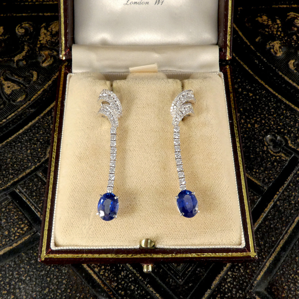 A close-up of the Sri Lankan Sapphire and Diamond drop earrings displayed elegantly in a vintage jewelry box, emphasizing the luxurious design and sparkling gemstones.