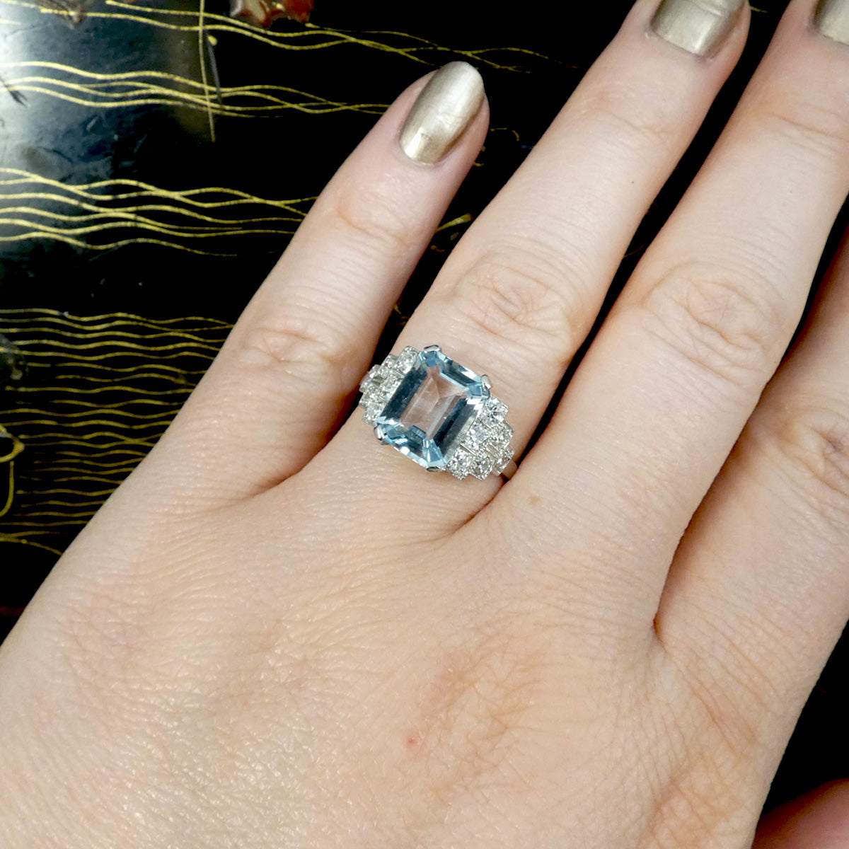 An Art Deco style ring that has been newly crafted with a 3.00ct light blue Aquamarine with graduated staged set Diamond shoulders in Platinum. Shown on finger for size and showing worn.