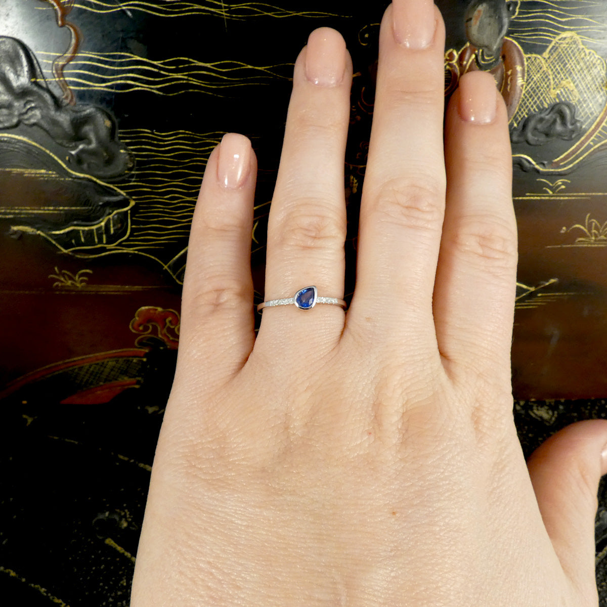 Pear cut Sapphire ring with diamonds set into the band shown on a hand to see size guide and how it will look when worn.