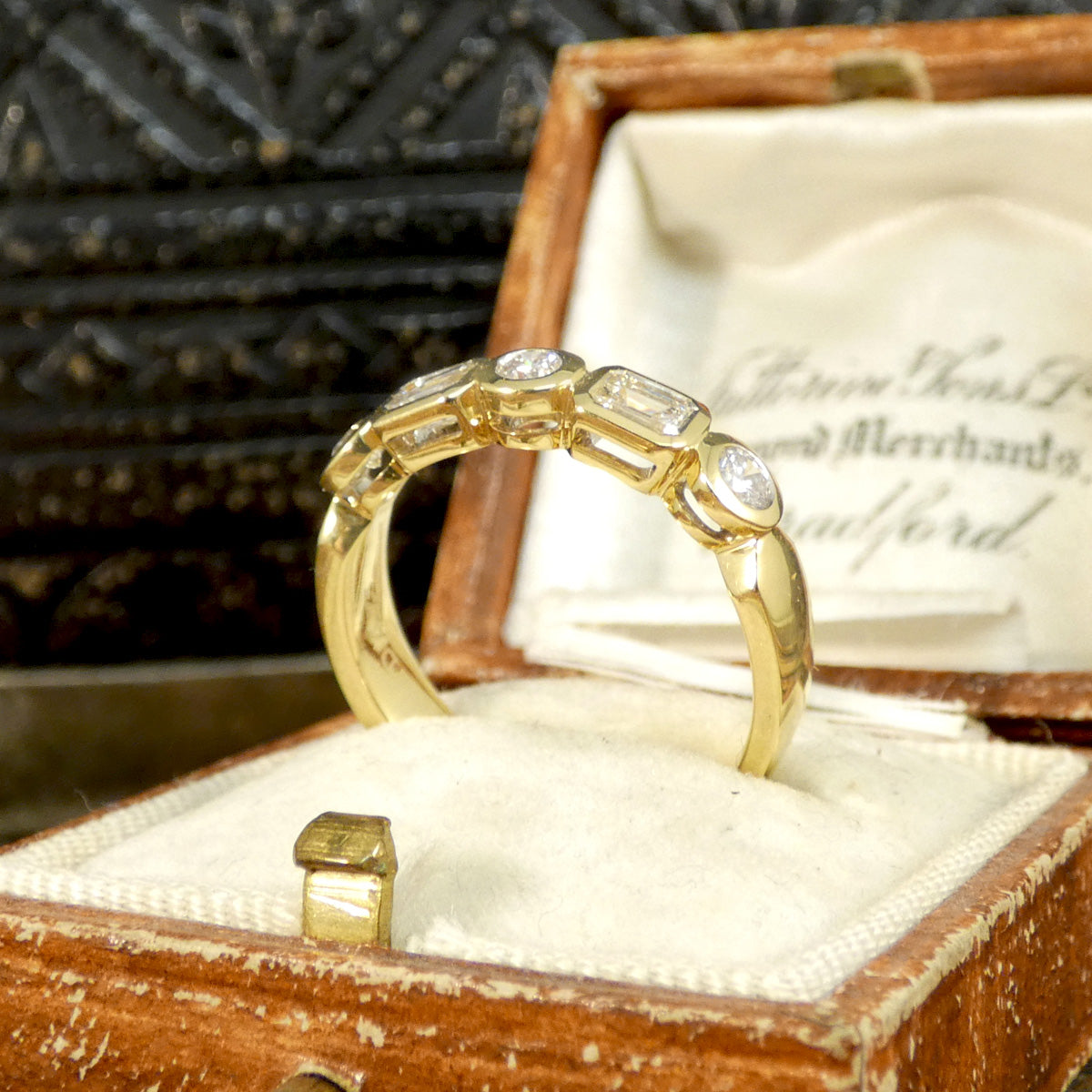  Half eternity ring with bezel-set emerald-cut and brilliant-cut diamonds in 18ct yellow gold, displayed in a vintage wooden ring box with a cream fabric interior. Showing side profile of gallery setting allowing light to pass through for the Diamonds to sparkle.