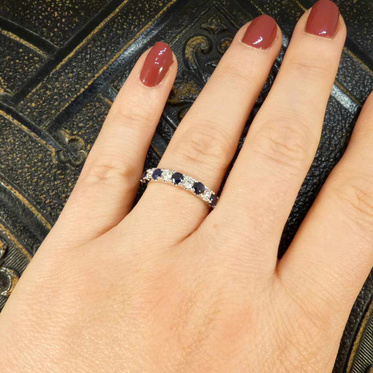 Alternating blue Sapphire and Diamond half eternity ring in white gold to complement the stones. Displayed on the finger when worn.