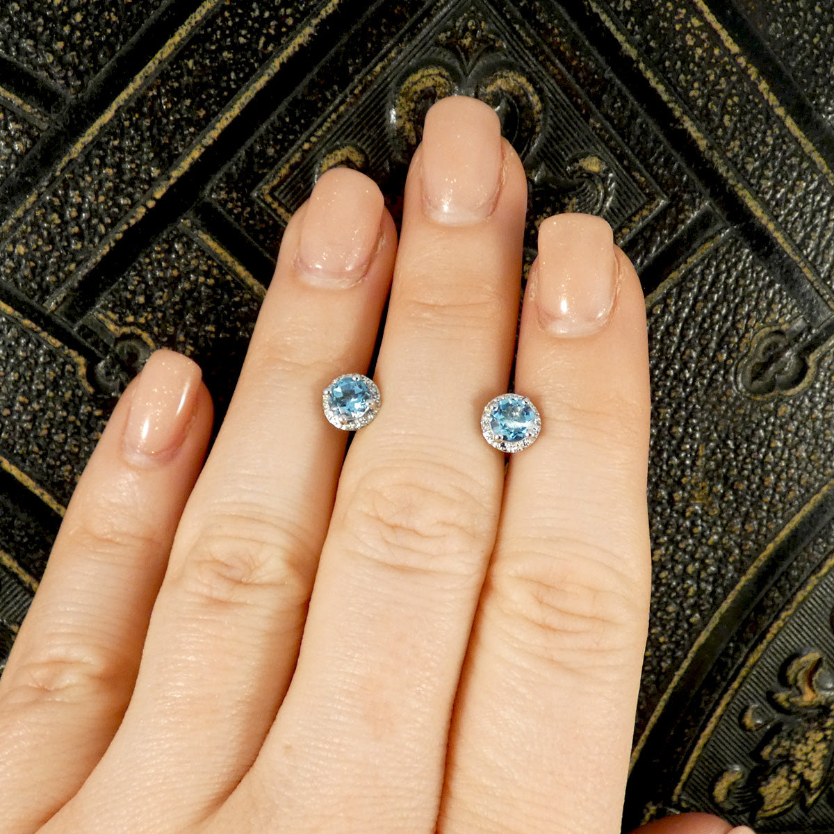 Blue Topaz stud earrings in white gold shown on a hand to show size ratio.