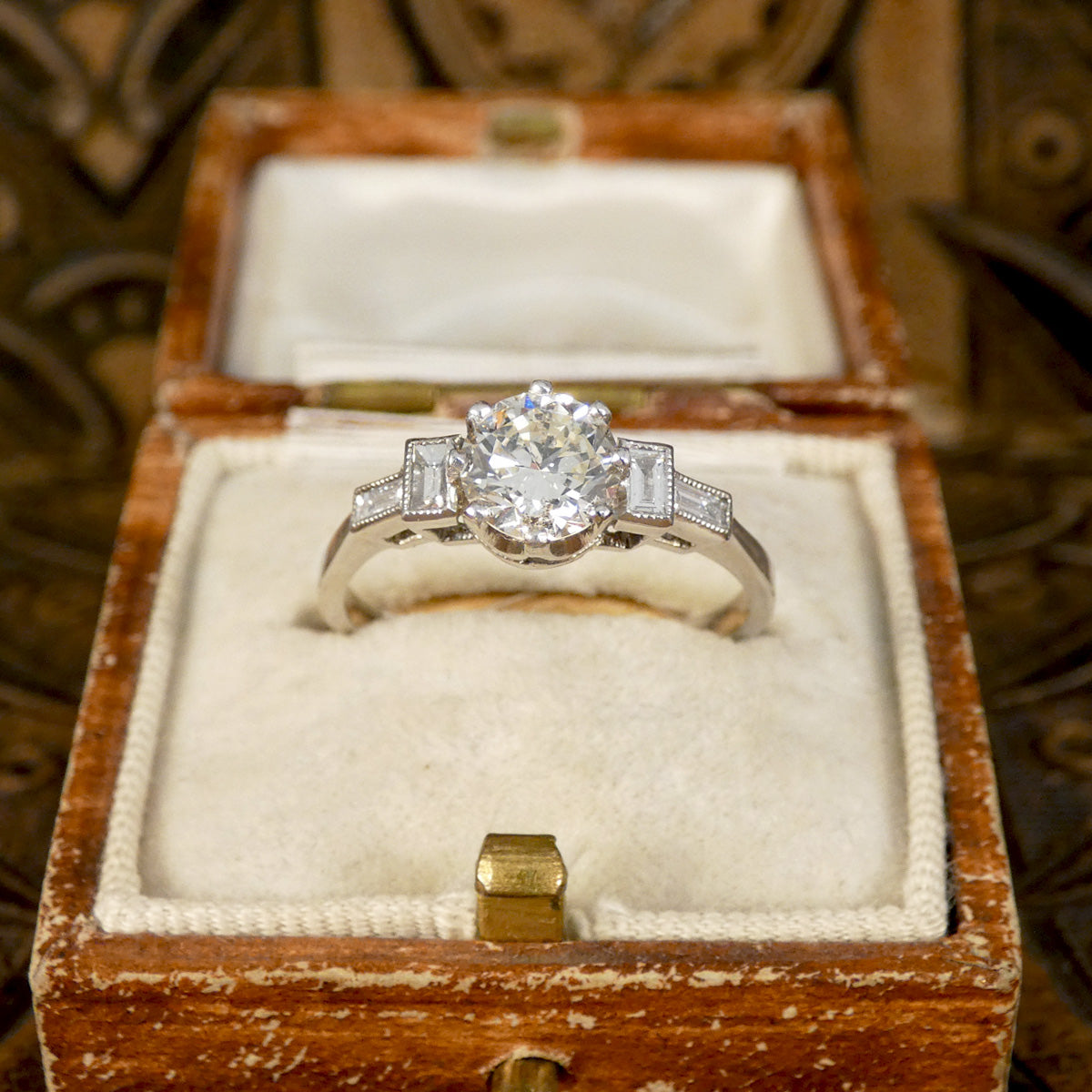 Art Deco homage engagement ring with an early brilliant cut centre and baguette cut diamond shoulders set in Platinum. Displayed in a vintage box.