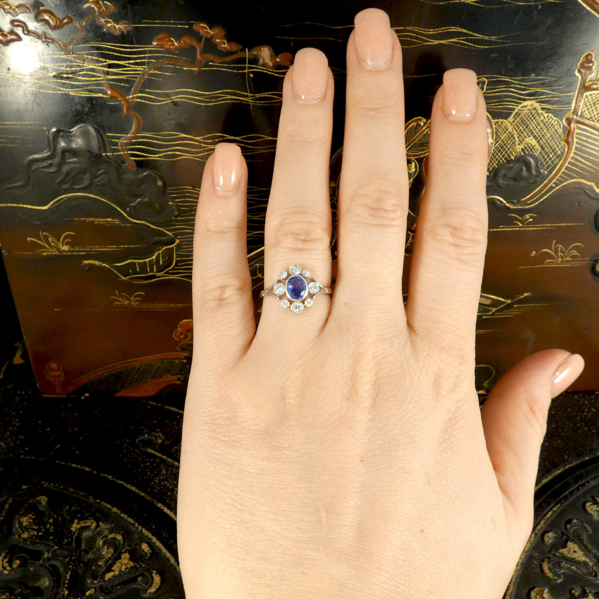 A platinum Sapphire and Diamond ring displayed on a hand, emphasising its elegant Art Deco-inspired design, with a vivid blue sapphire surrounded by sparkling diamonds.