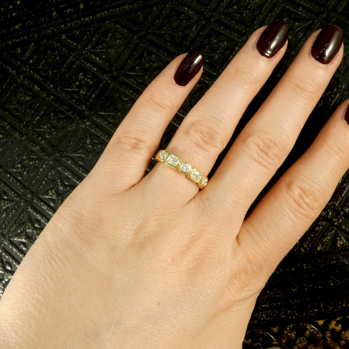  Half eternity ring with bezel-set emerald-cut and brilliant-cut diamonds in 18ct yellow gold, displayed on a hand to see ring in use and worn on the finger.