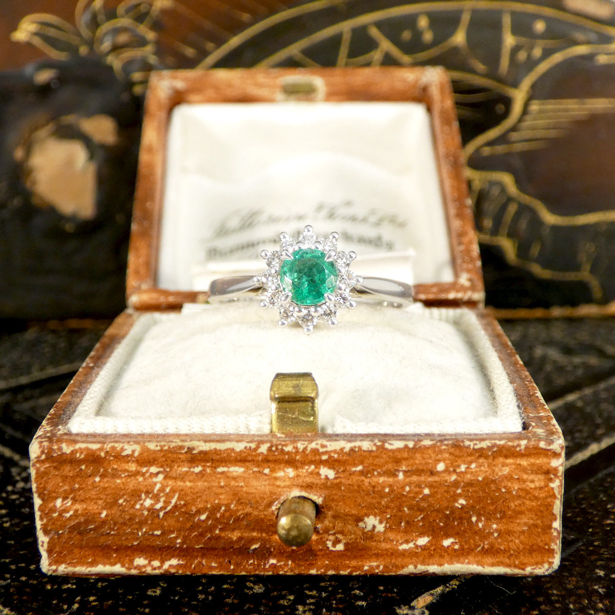 Emerald and diamond flower cluster ring in platinum elegantly displayed in a vintage jewellery box, showcasing its luxurious and timeless design.