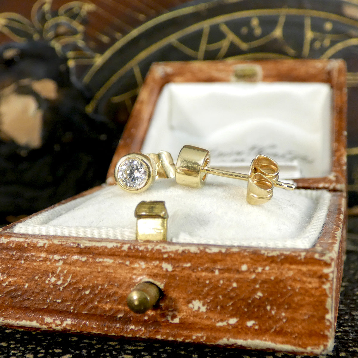 Close-up view of 0.40ct brilliant-cut diamond stud earrings in a vintage box, showcasing their elegant yellow gold bezel setting and secure post design.