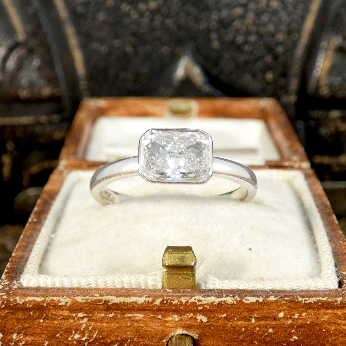 Radiant cut east-west bezel set solitaire engagement ring in 18ct white gold, featuring a G-colour diamond with a calculated weight of 1.29ct, elegantly displayed in a vintage wooden ring box.