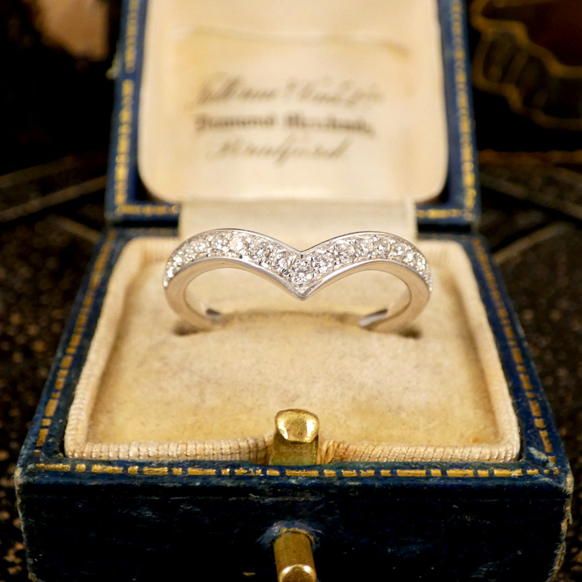 Diamond set wishbone ring displayed in an antique box from front profile.