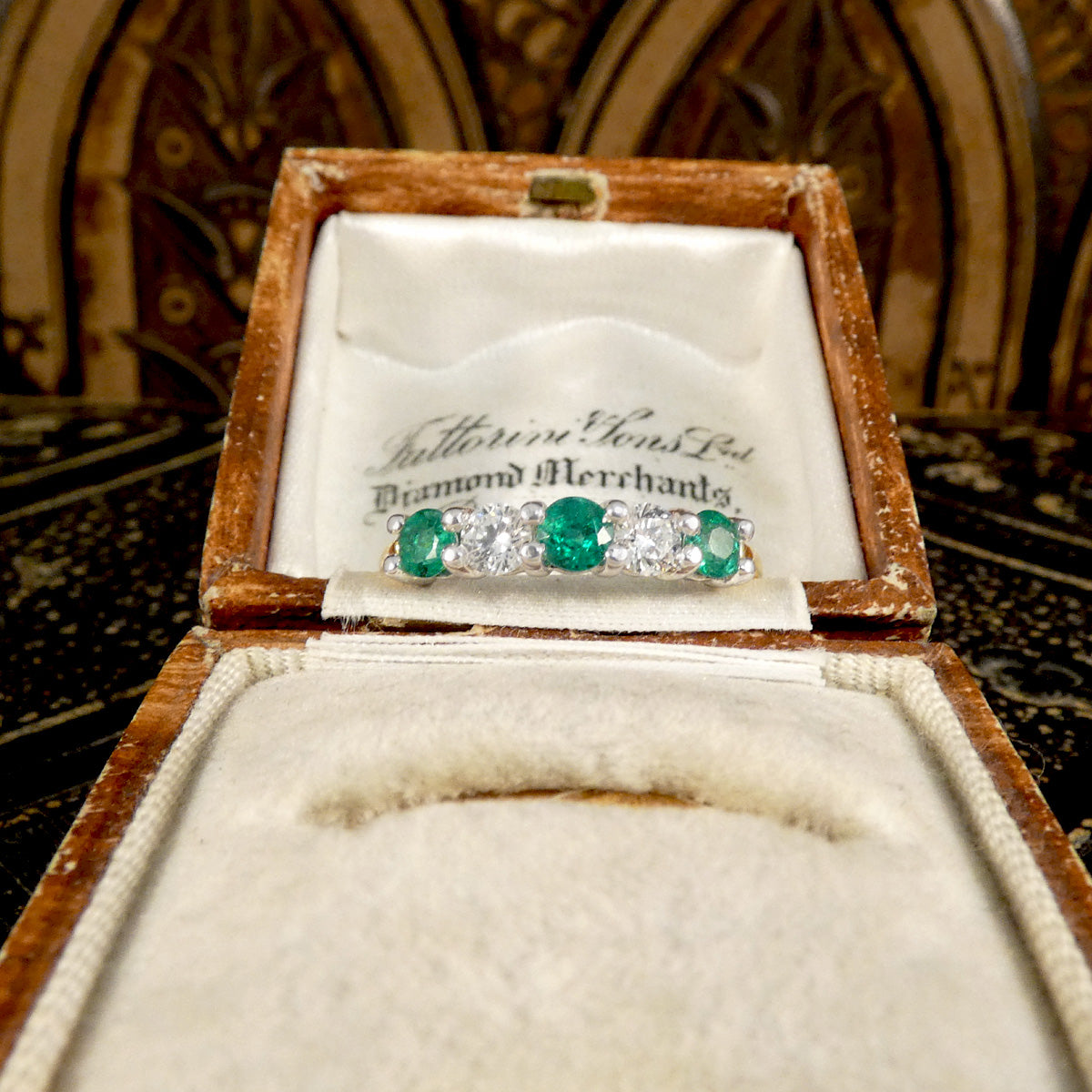 Featuring bright and vibrant emeralds sandwiching bright and clear diamonds in a five stone band ring in a vintage box.