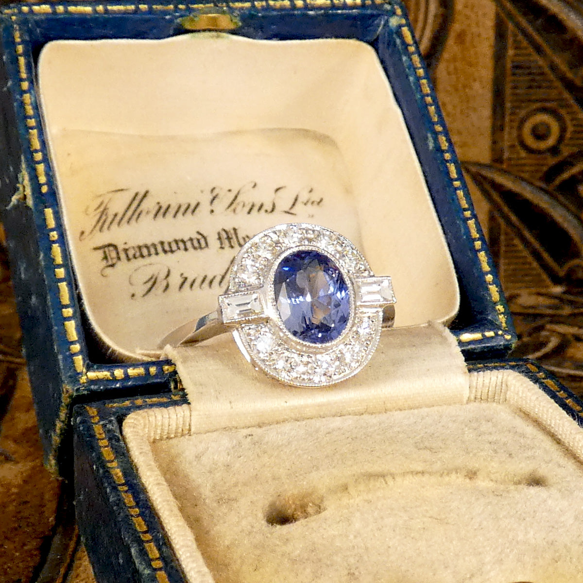 An oval cut Sapphire with a rub over bezel setting surrounded by Brilliant and Baguette cut Diamonds clustering the velvet blue centre stone. A true are deco style ring, a beautiful vintage classic. Displayed in vintage box.