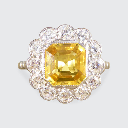 Art Deco-style ring featuring a stunning 2.10ct Asscher cut yellow sapphire, encircled by sparkling diamonds in a timeless cluster design.